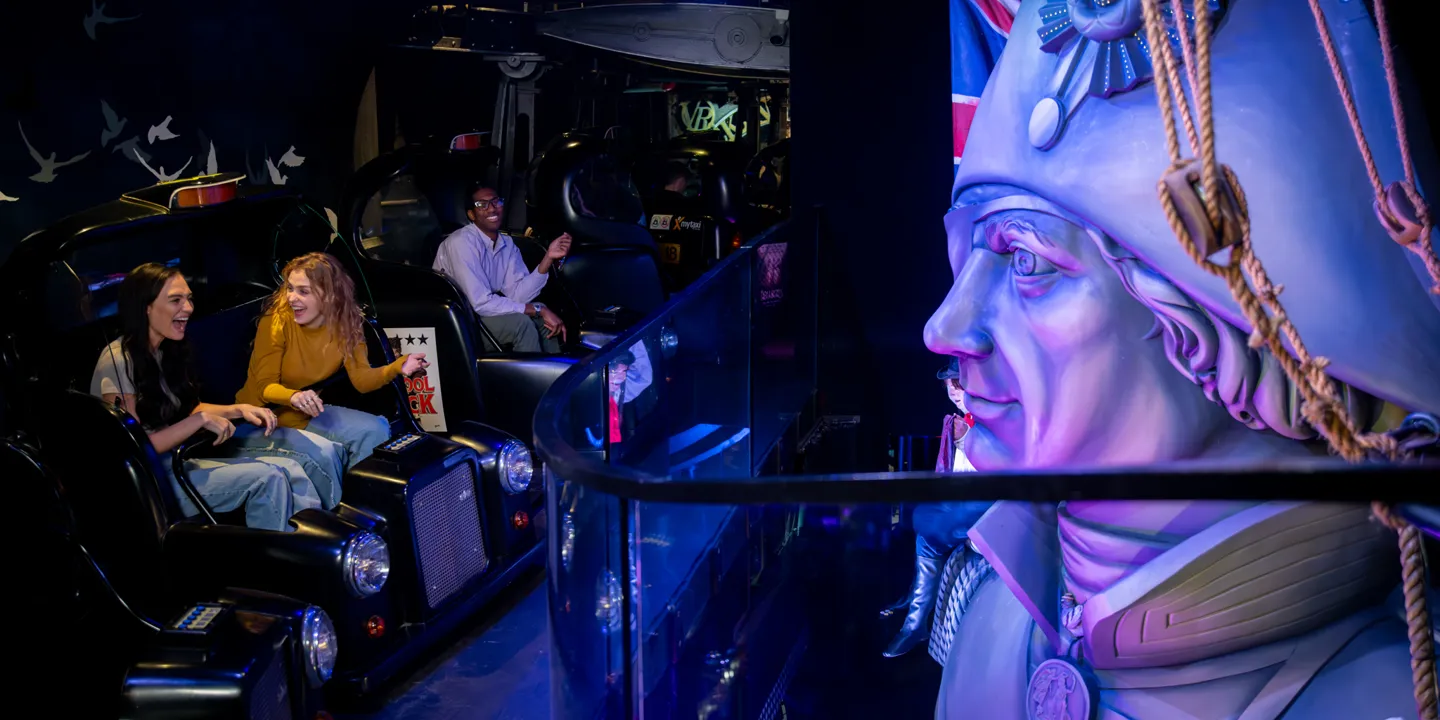 People sitting in taxi cabs on the Spirit of London ride at Madame Tussauds London, pointing at a recreation of Nelson's Column