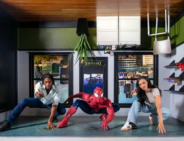 Two people posing alongside Spiderman in a bedroom set